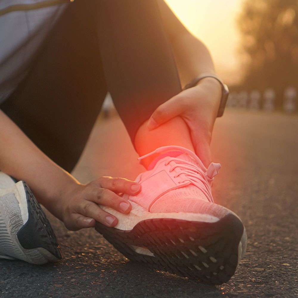 A person sitting on a road holding their ankle, which is highlighted with a red glow to indicate pain or injury.
