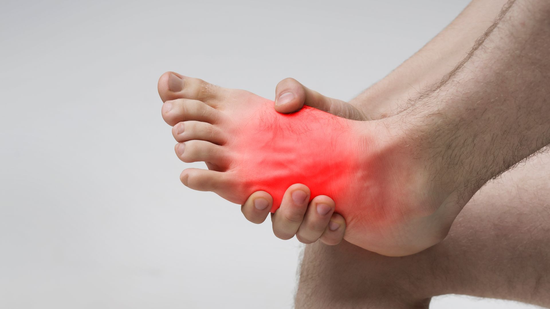 A person holding their foot, which is highlighted in red to indicate pain or inflammation.