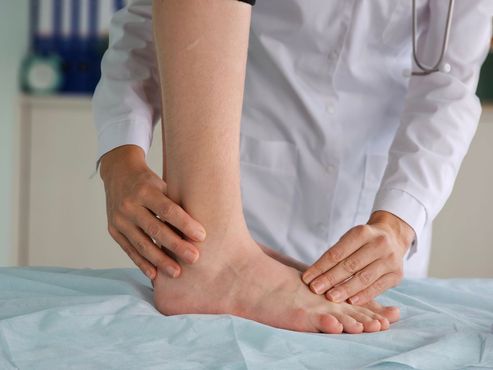 A healthcare professional in a white coat performing a physical examination on a patient's ankle.