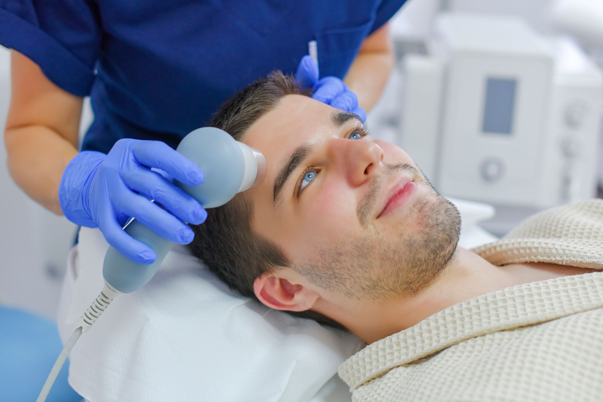 Scalp treatment performed with handheld device by clinician in medical aesthetic clinic.