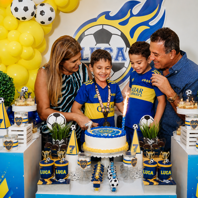 Children and adults at a blue-and-yellow soccer birthday party around a cake and decorations