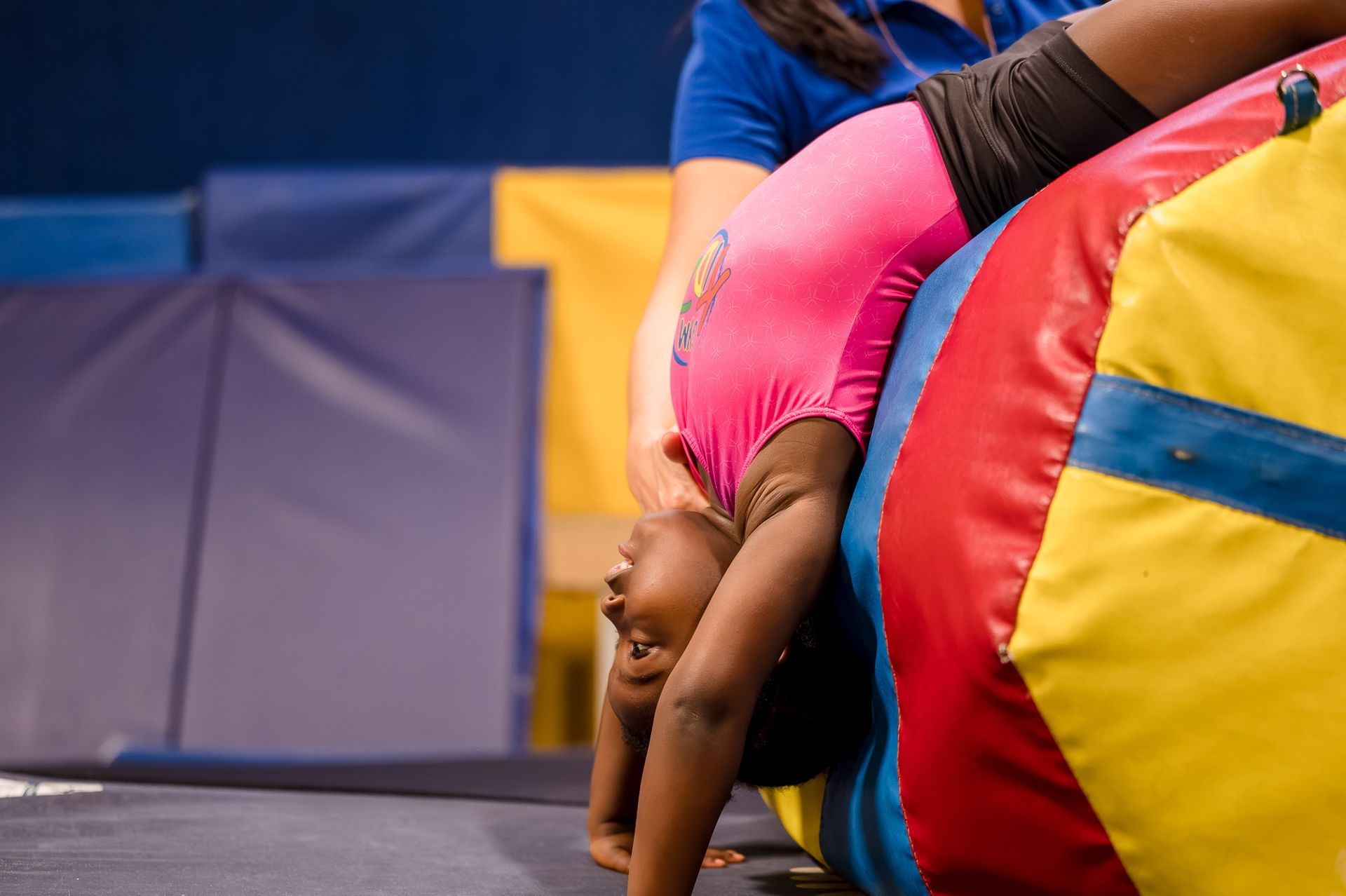 Child bent backward in a gym, touching the floor beside colorful padded mats