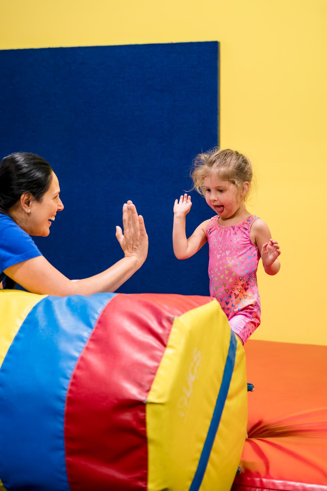 Adult and child high-five in a colorful playroom with a blue wall and yellow floor mats.