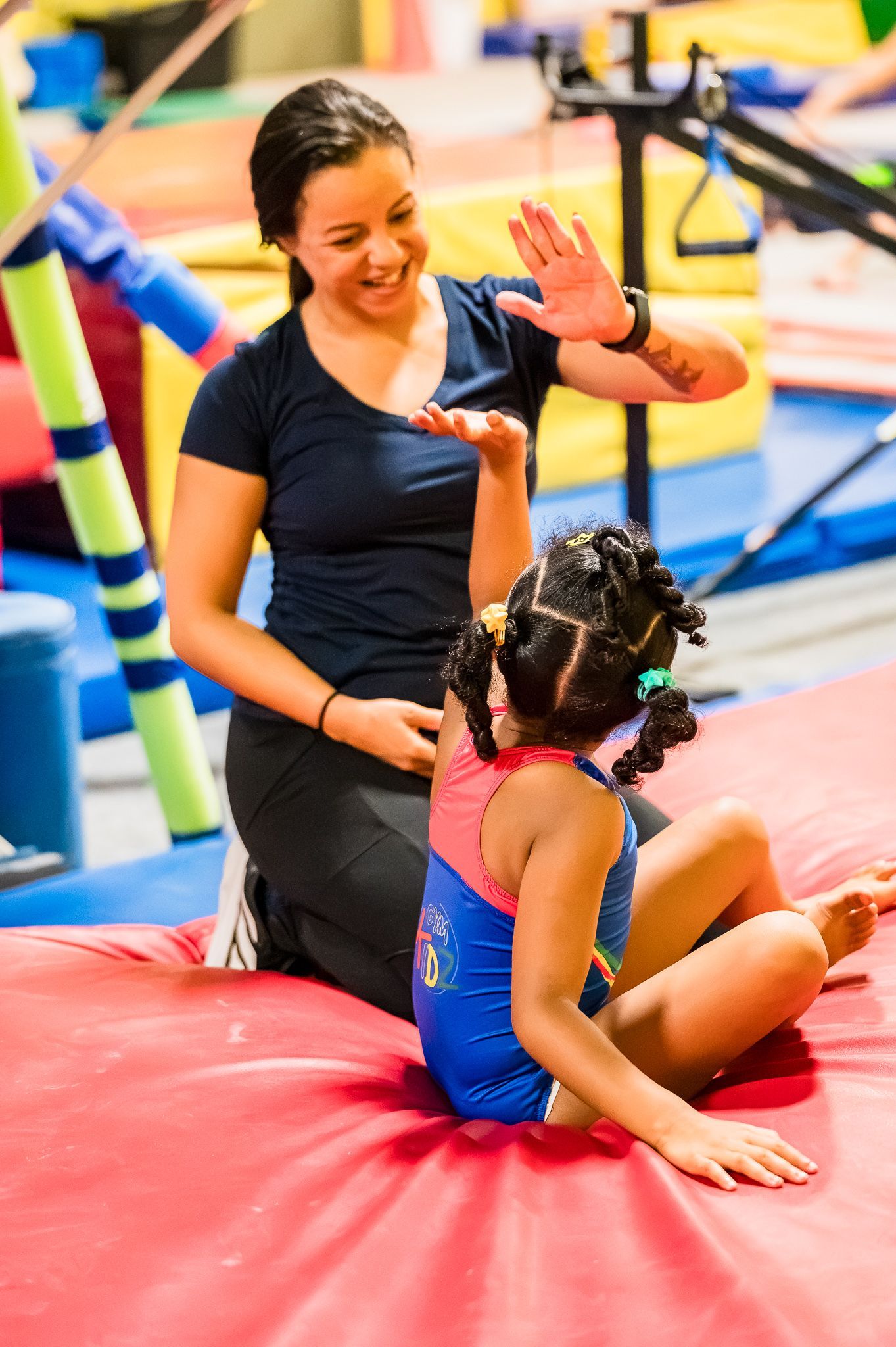 Coach high-fiving a child on a red gym mat during an indoor play session