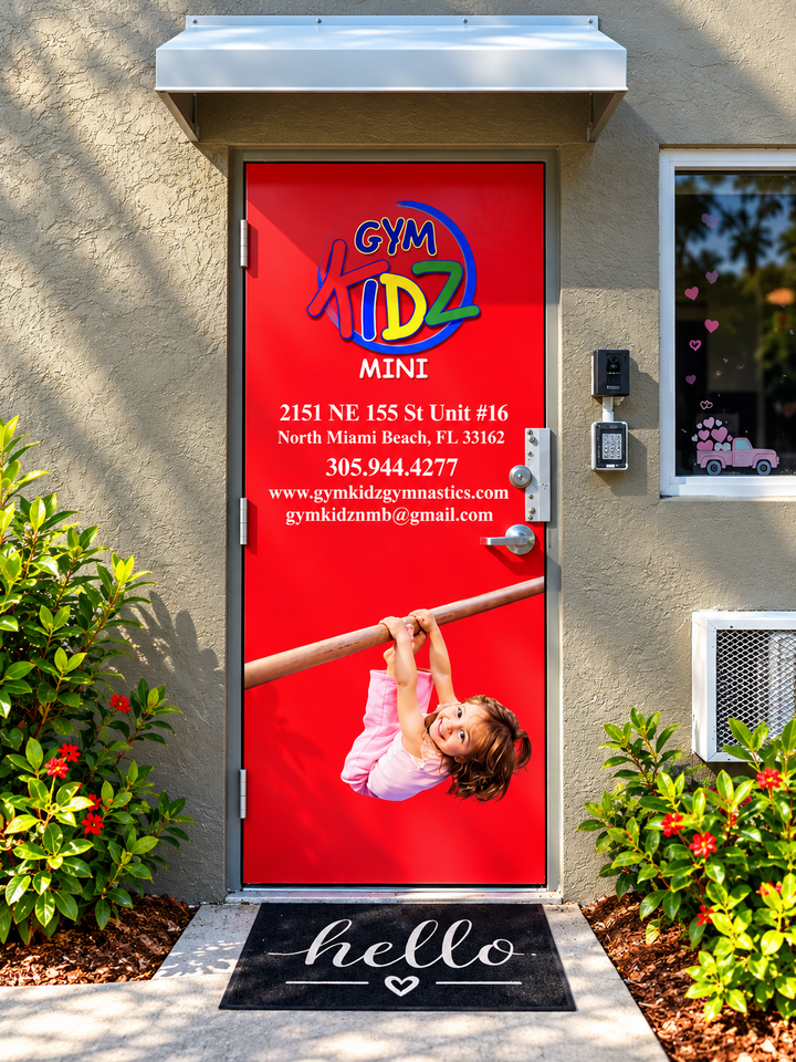 Bright red daycare door with child logo, white text, and a child swinging on a bar beneath a “hello” doormat.