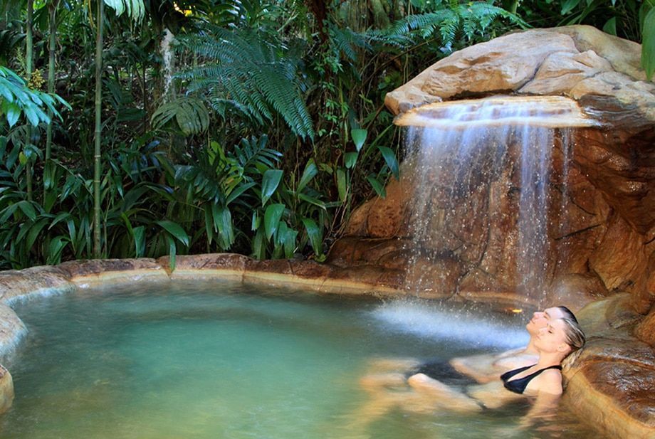 A woman is laying in a hot tub under a waterfall.