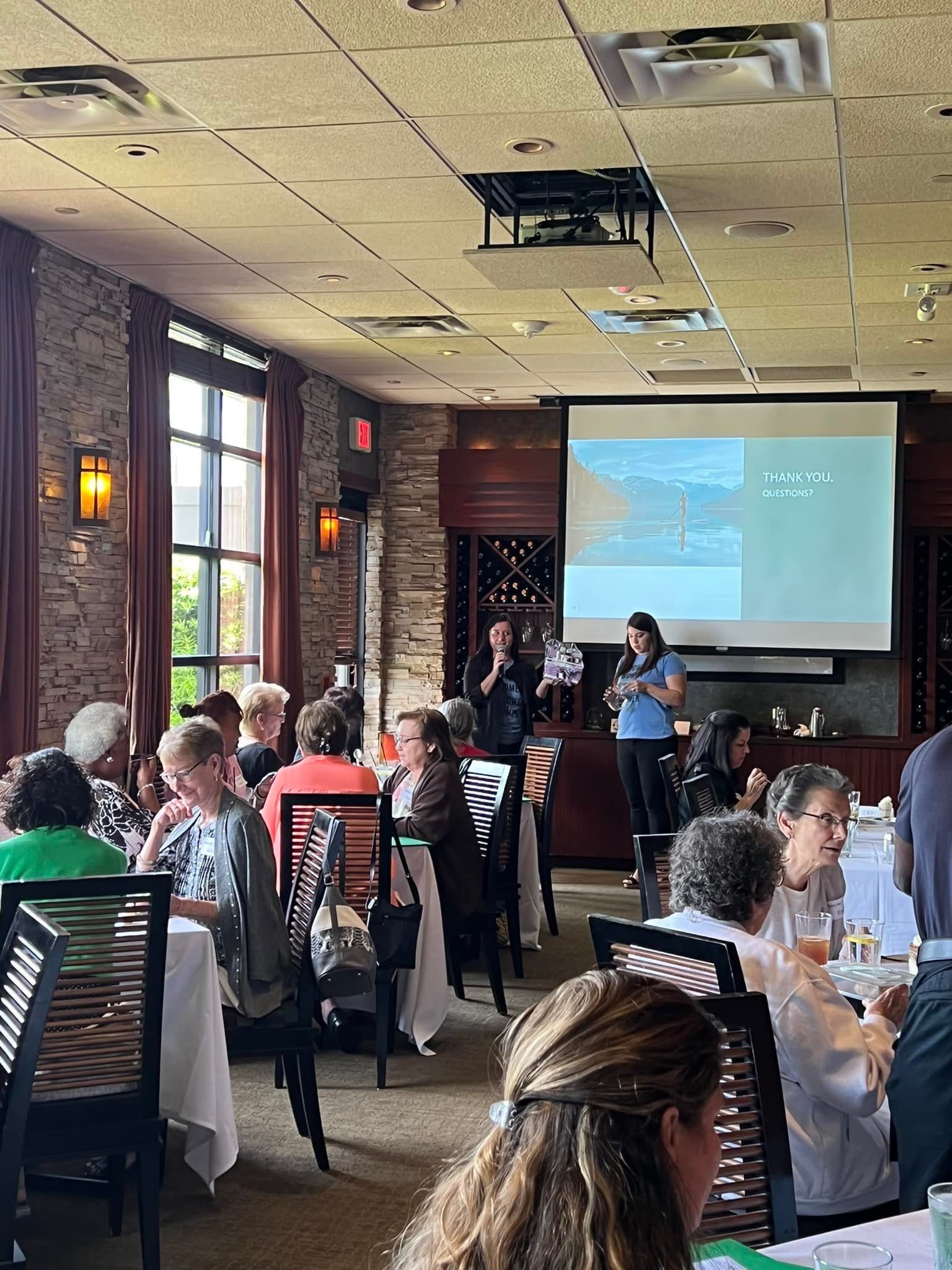 A group of people are sitting at tables in a restaurant watching a presentation.