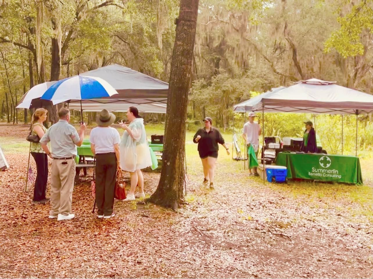A group of people are standing under tents in a park.
