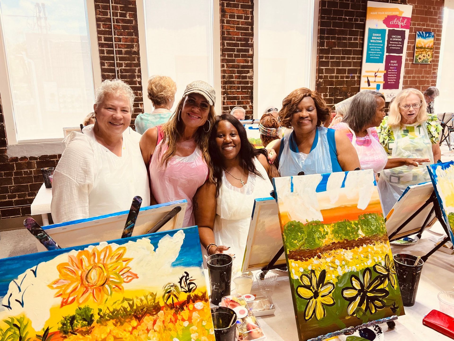 A group of women are posing for a picture in front of paintings.