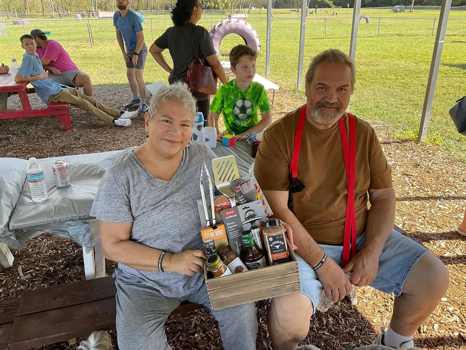 A man and a woman are sitting on a bench holding a box of food.