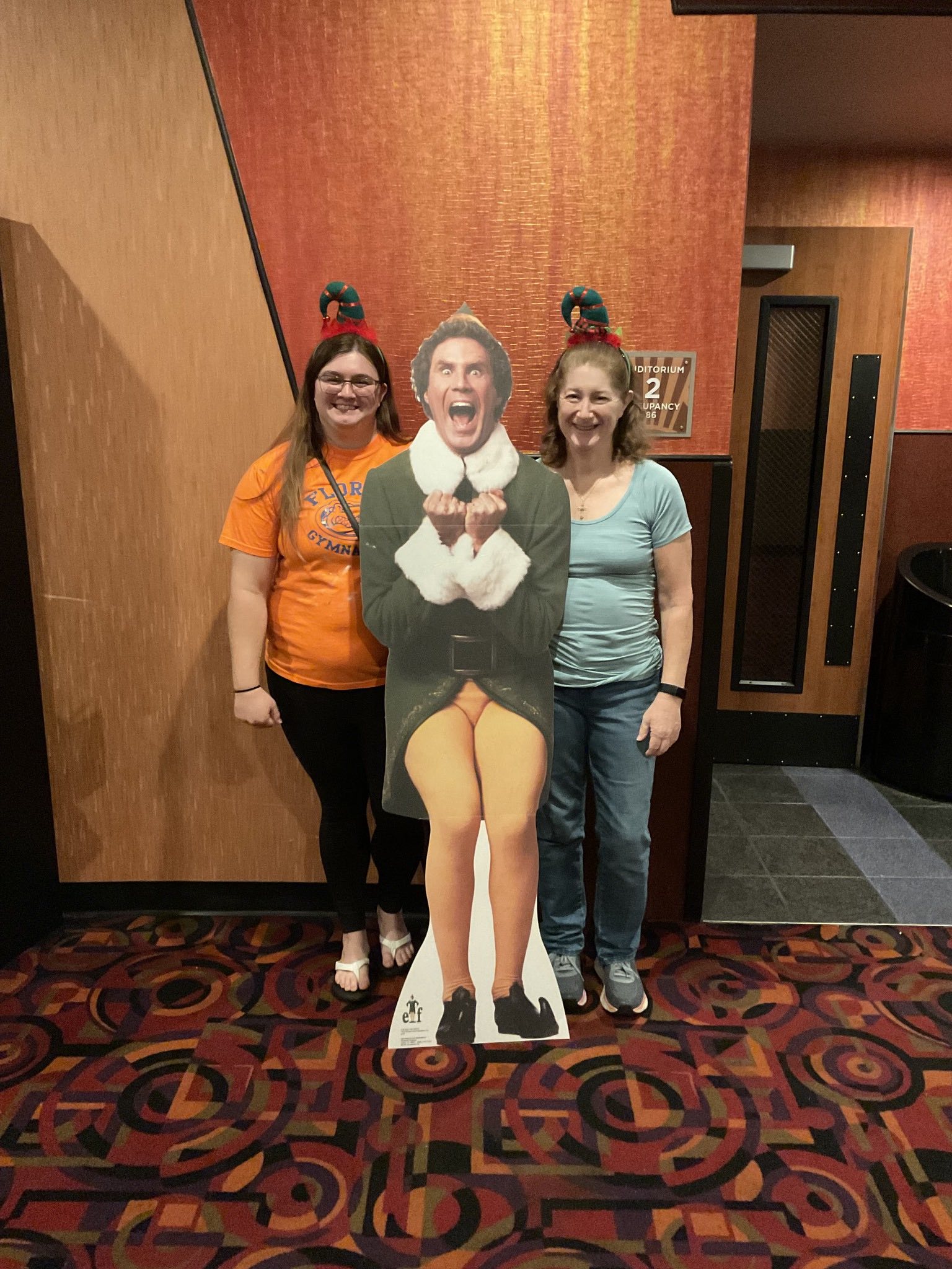 Two women are standing next to a cardboard cutout of elf.