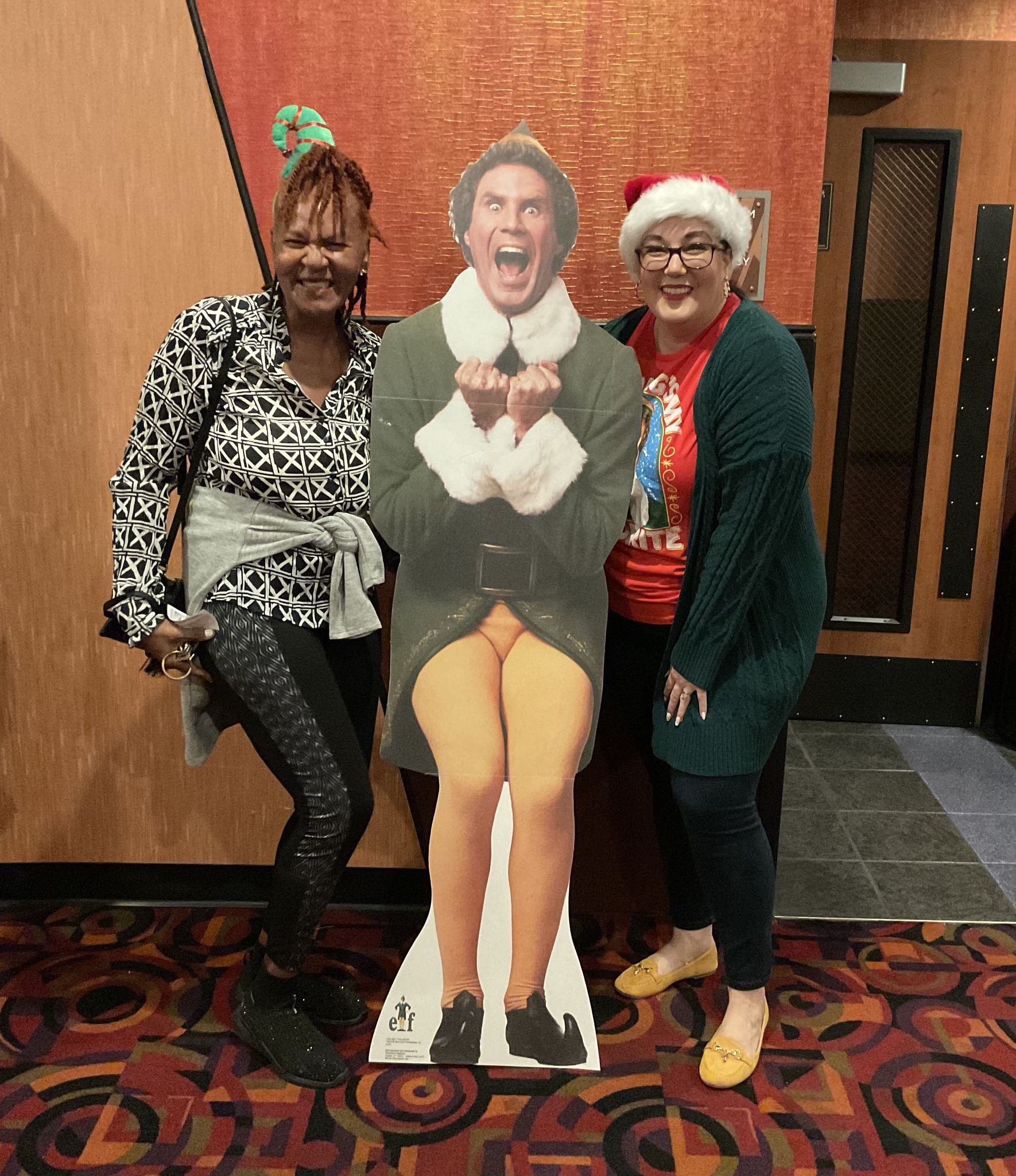 Two women standing next to a cardboard cutout of elf