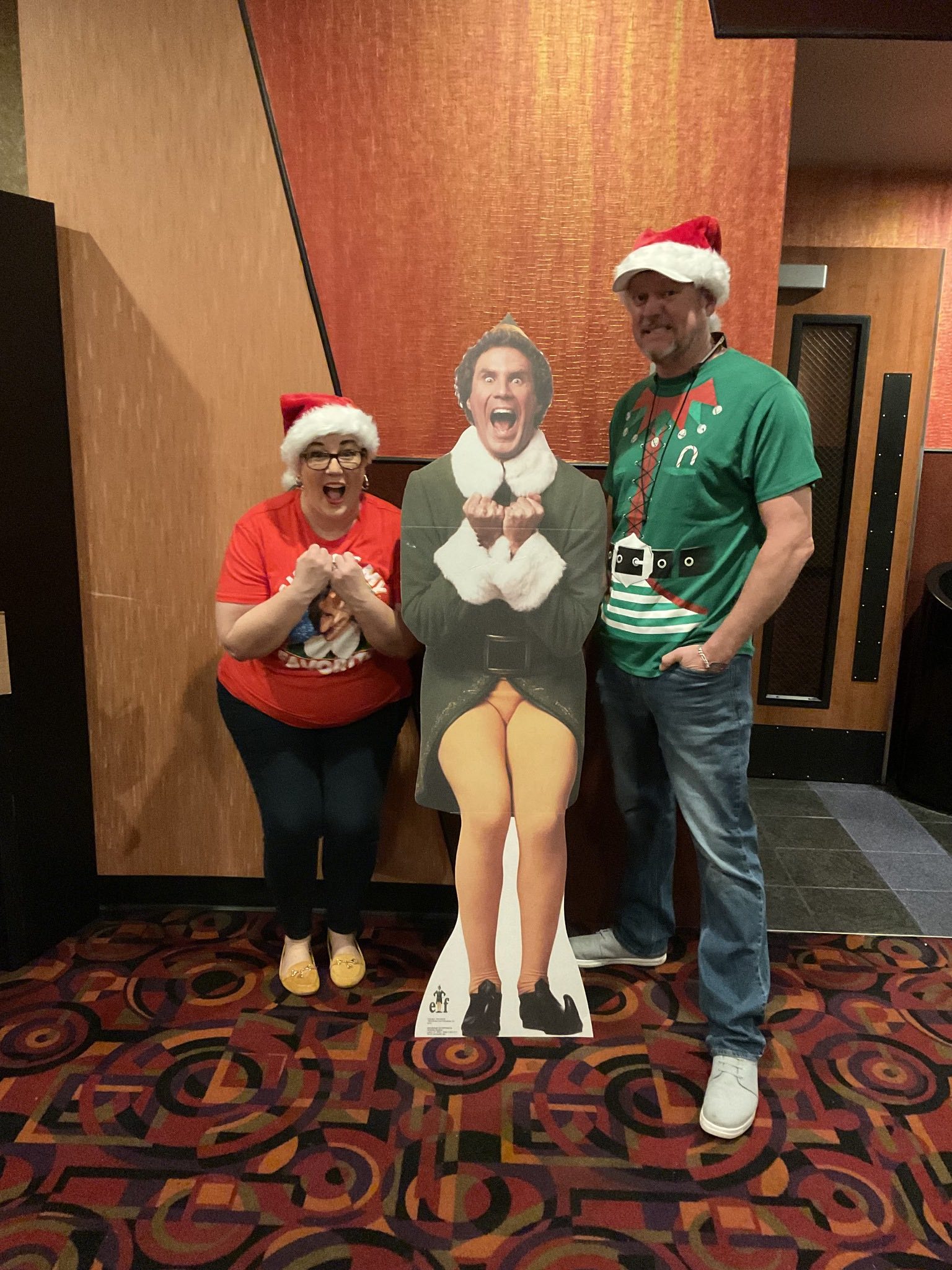 A man and a woman are standing next to a cardboard cutout of elf.
