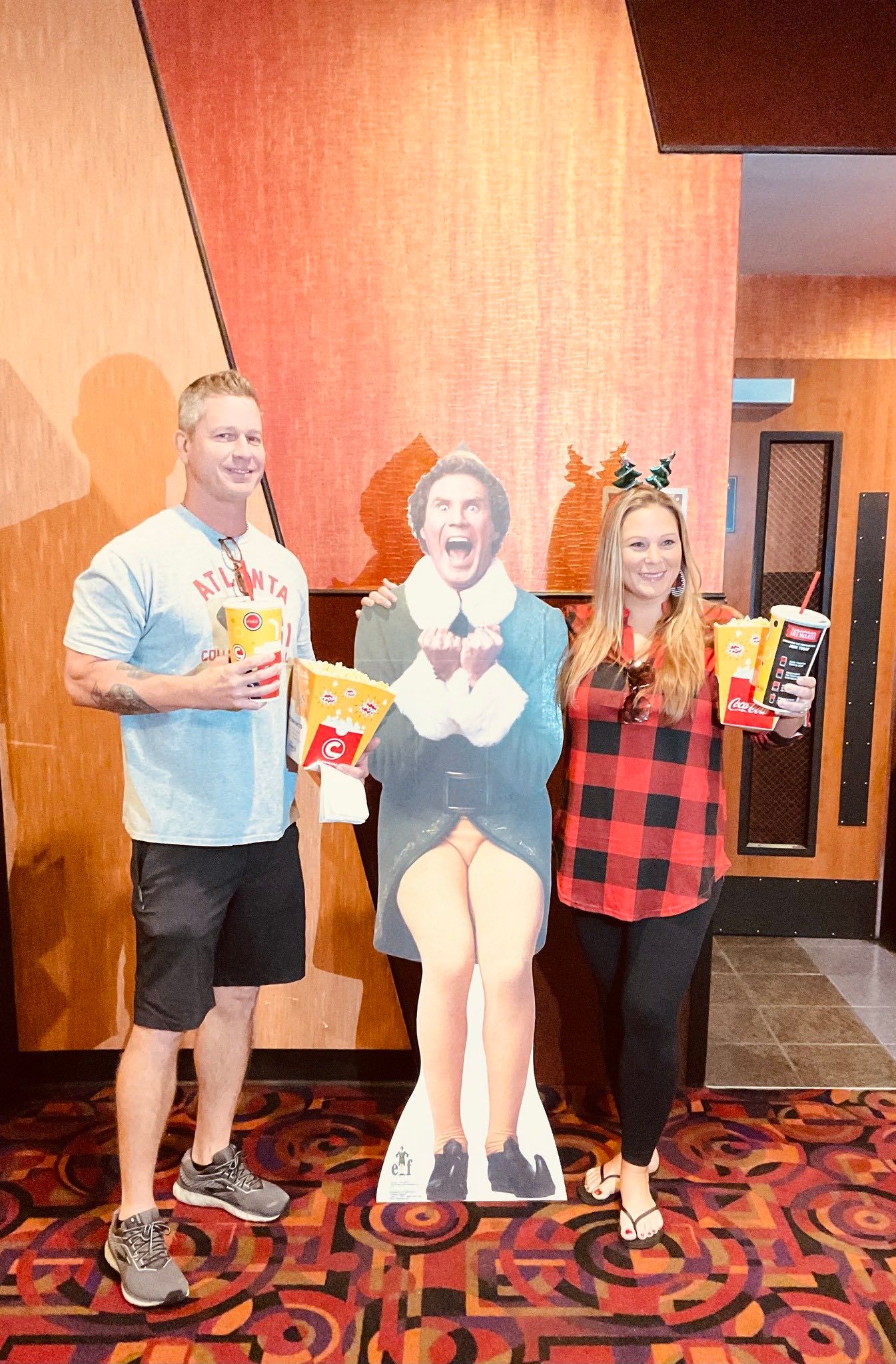 A man and a woman are standing next to a cardboard cutout of eddie the elf.
