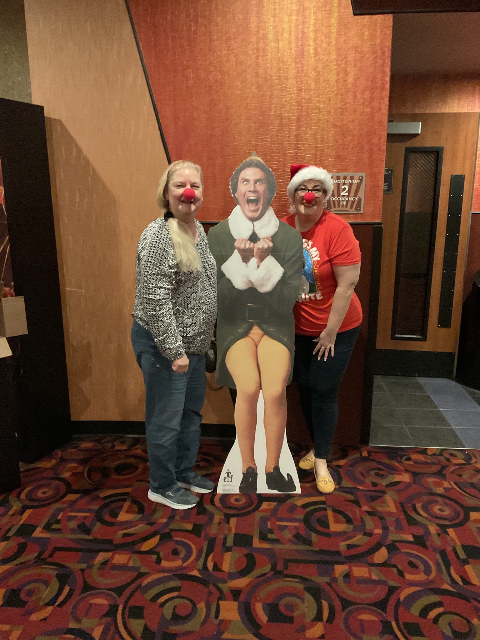 Two women are standing next to a cardboard cutout of a man with red noses.