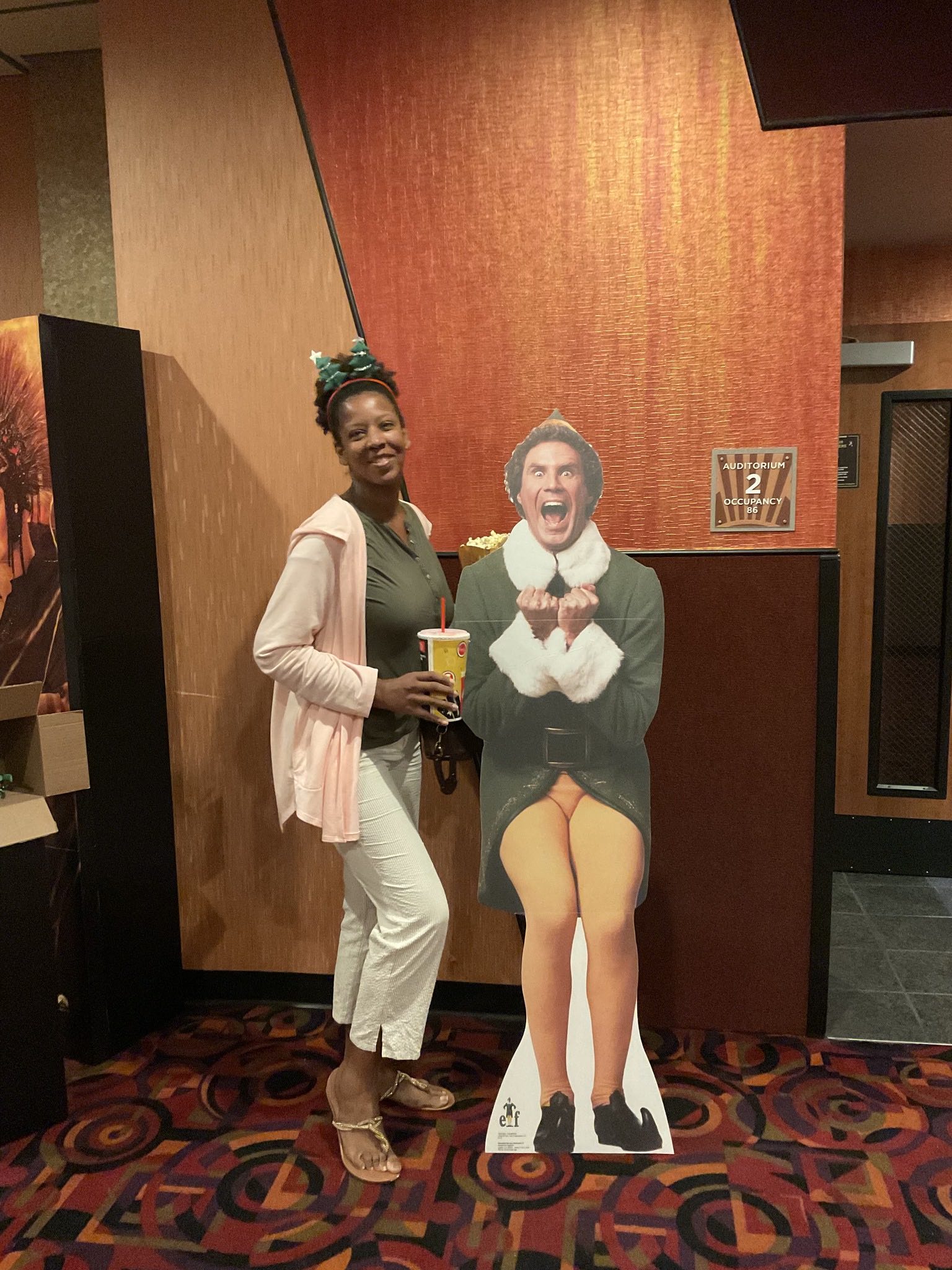 A woman is standing next to a cardboard cutout of elf
