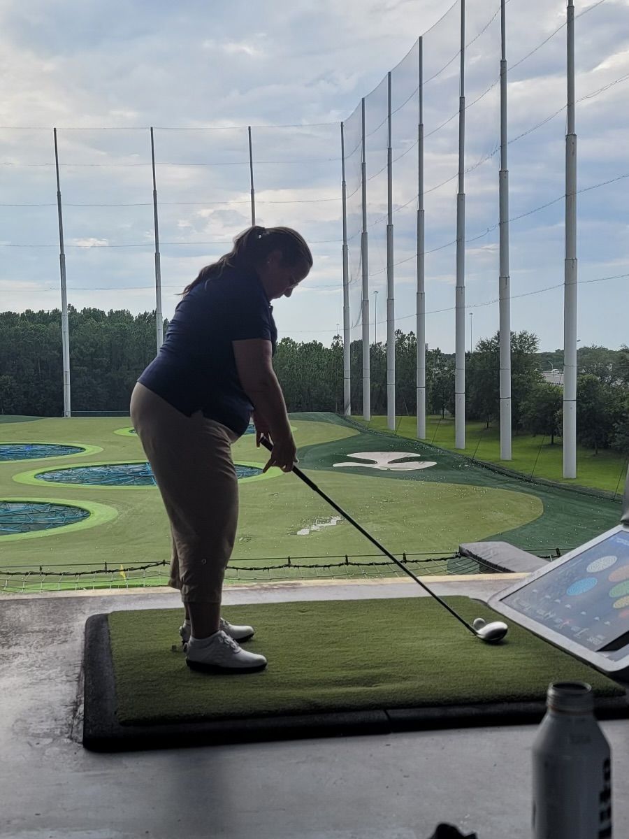A woman is swinging a golf club on a driving range