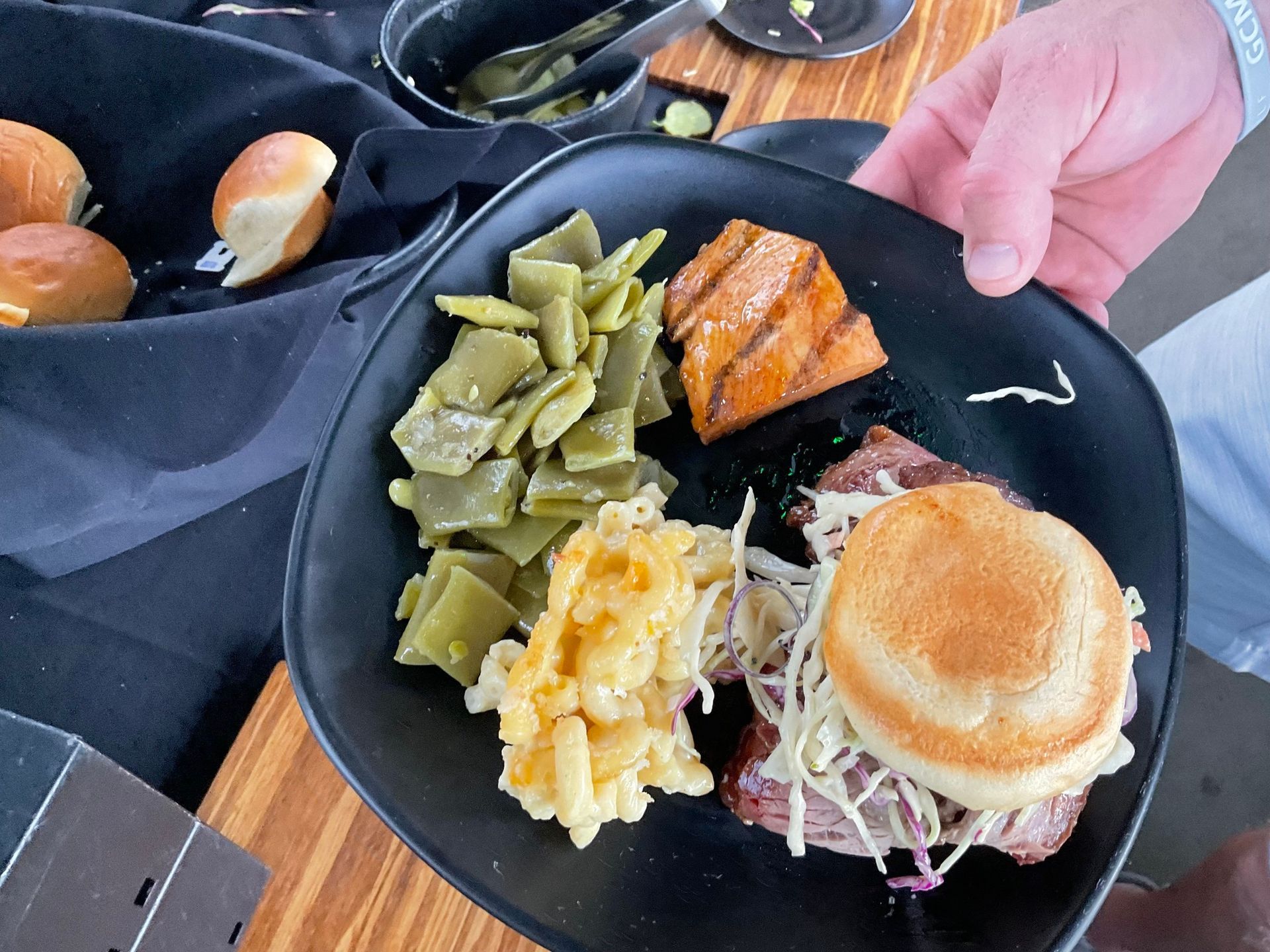 A person is holding a plate of food with green beans , macaroni and cheese and a sandwich.