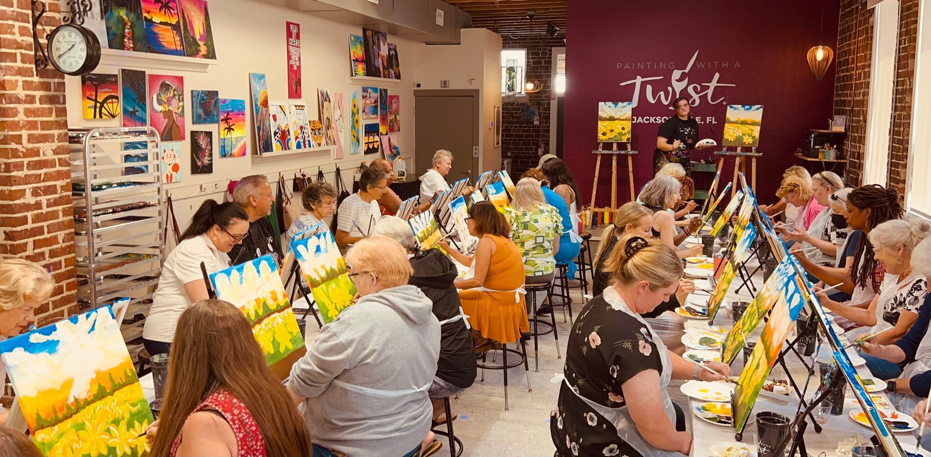 A large group of people are sitting at tables in a room painting.