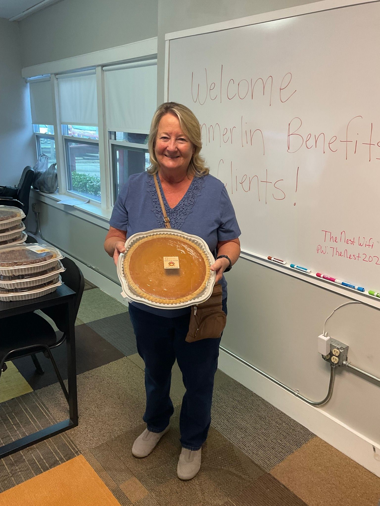 A woman is holding a pie in front of a whiteboard.