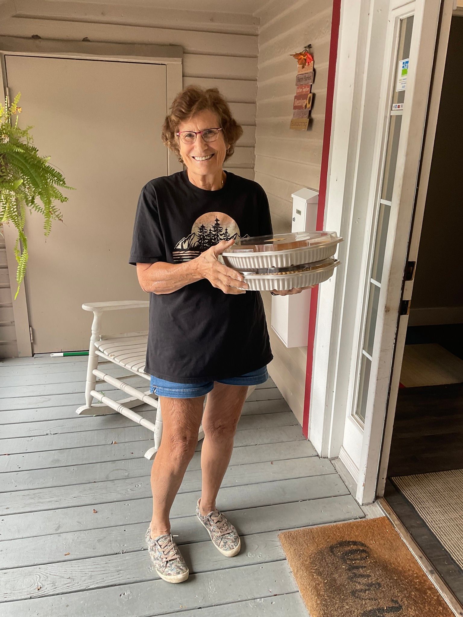 A woman is standing on a porch holding a tray of food.