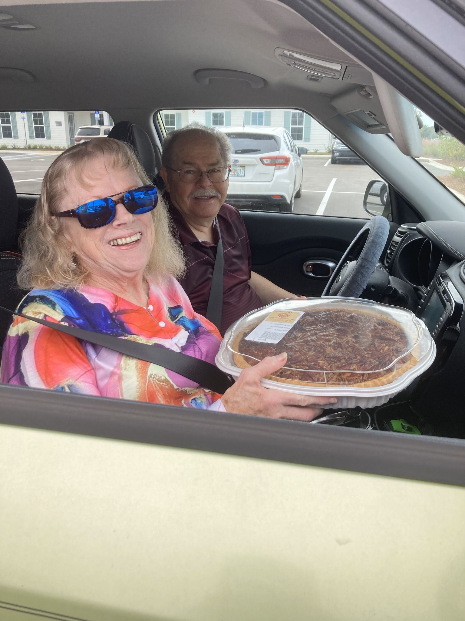 A man and a woman are sitting in a car holding a pie.