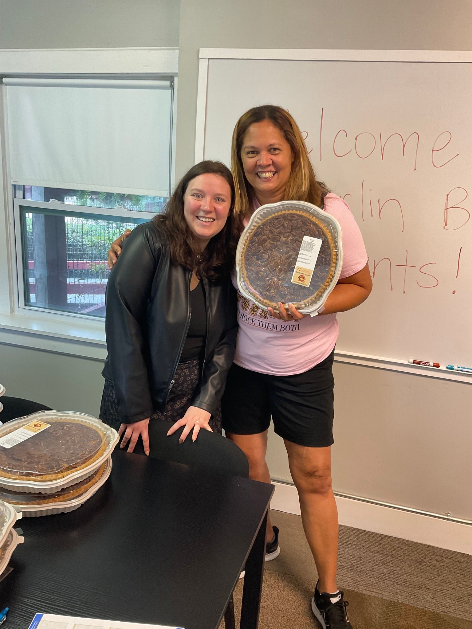 Two women are standing next to each other holding a pie.