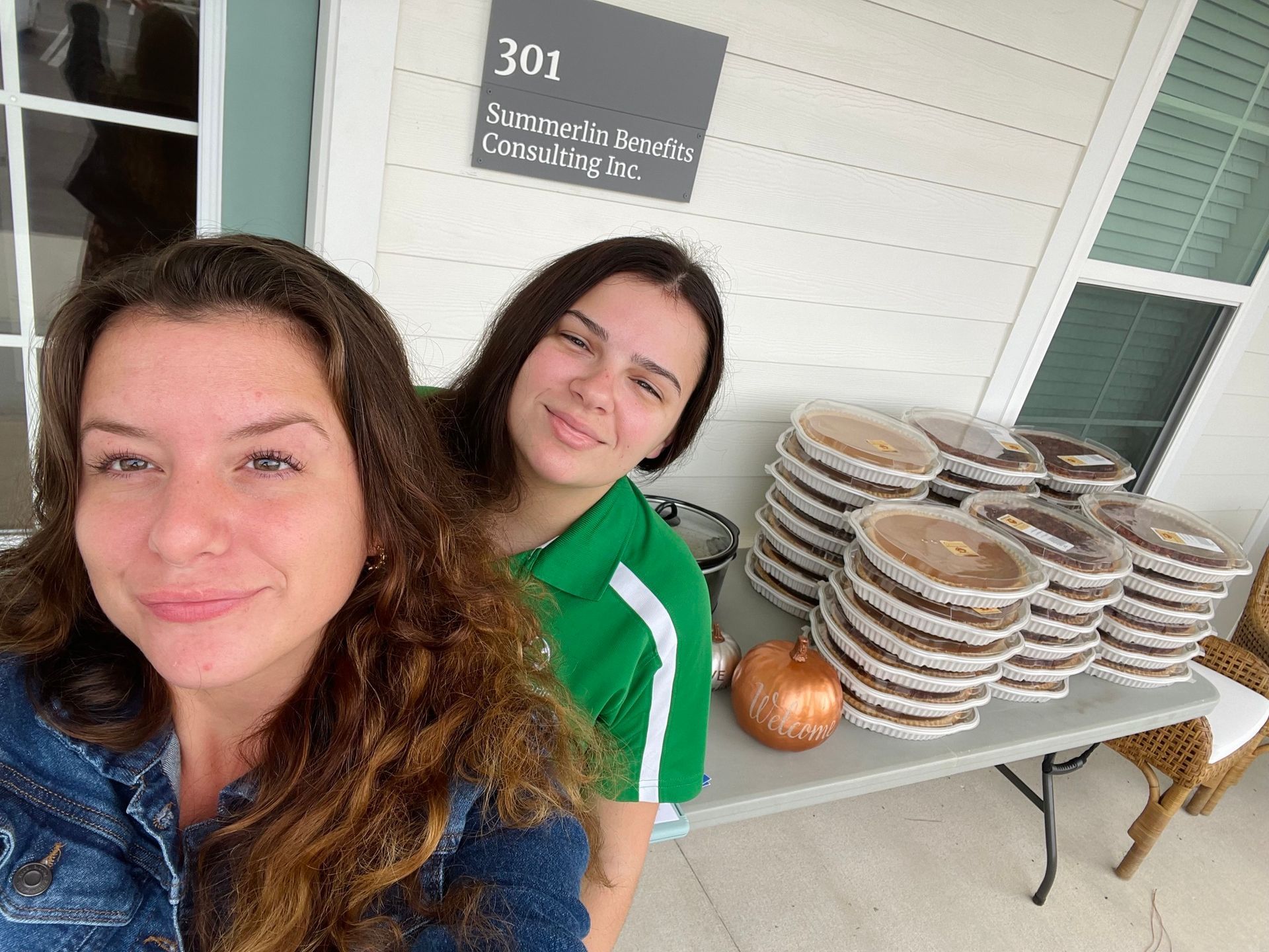 Two women are posing for a picture in front of a table full of pies.