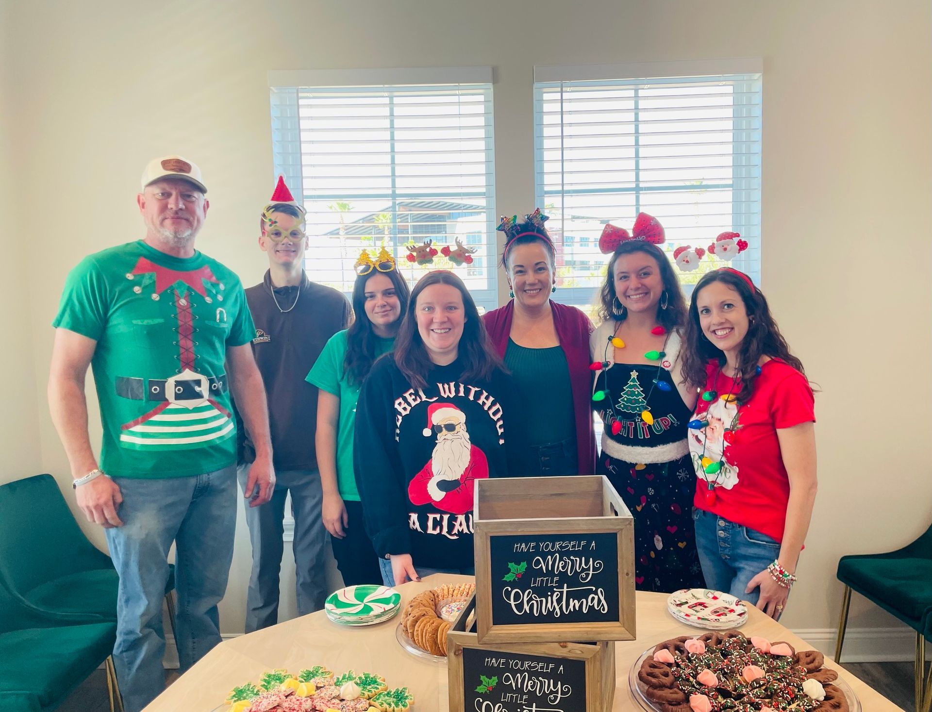 A group of people wearing christmas sweaters are standing around a table.