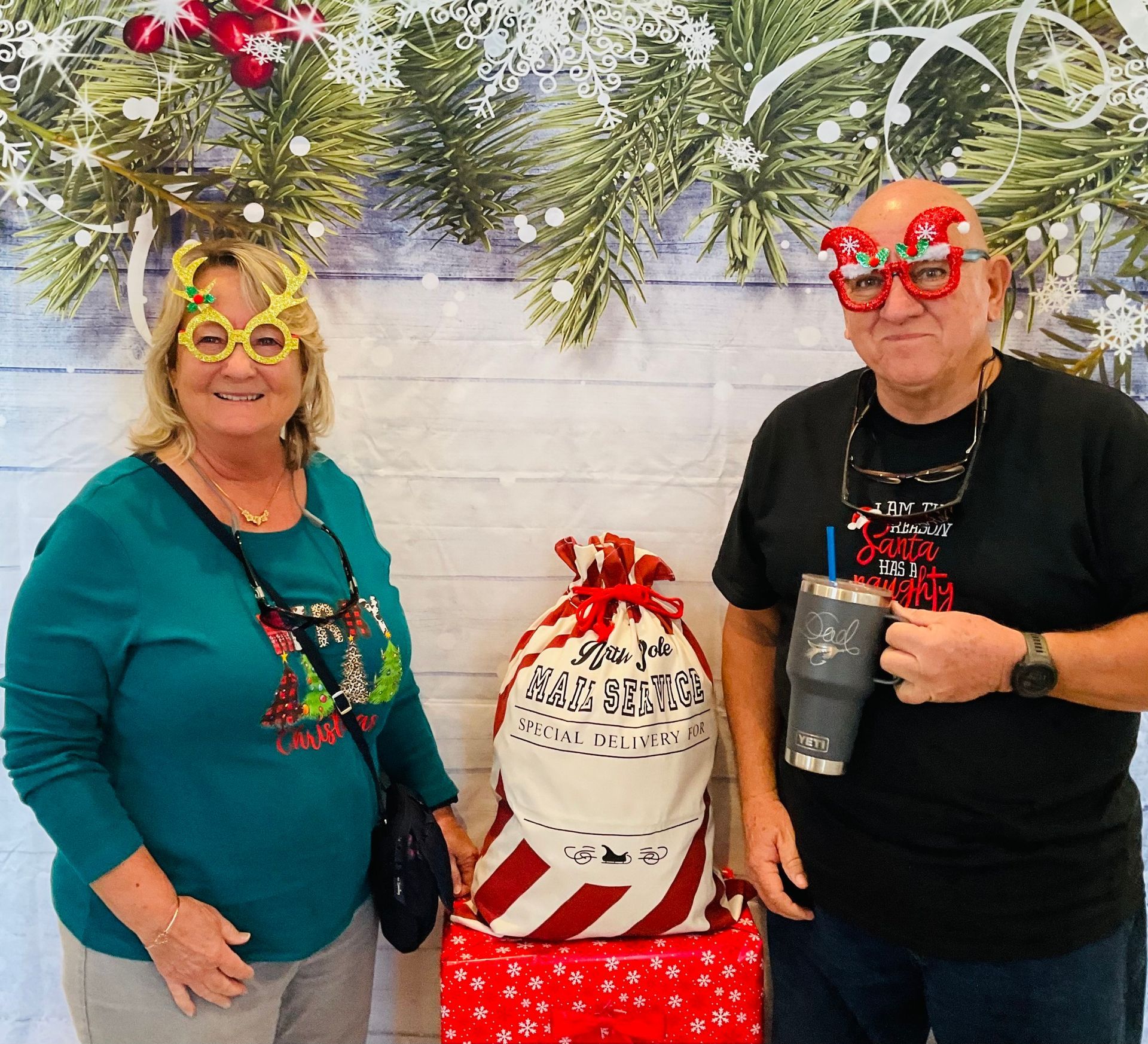 A man and a woman are posing for a picture in front of a christmas backdrop.