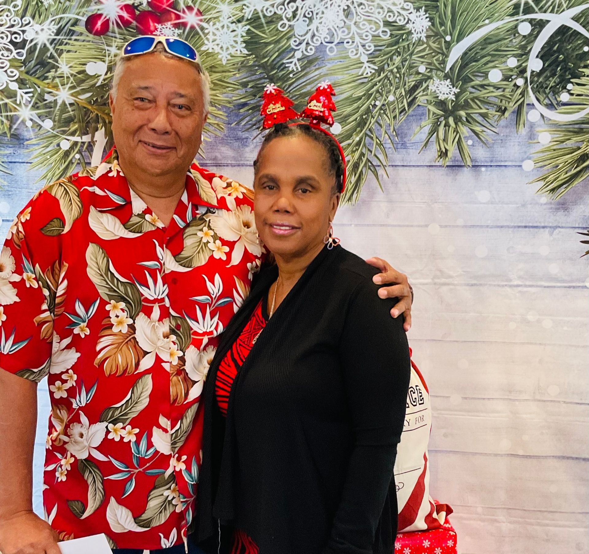 A man and a woman are posing for a picture in front of a christmas background.