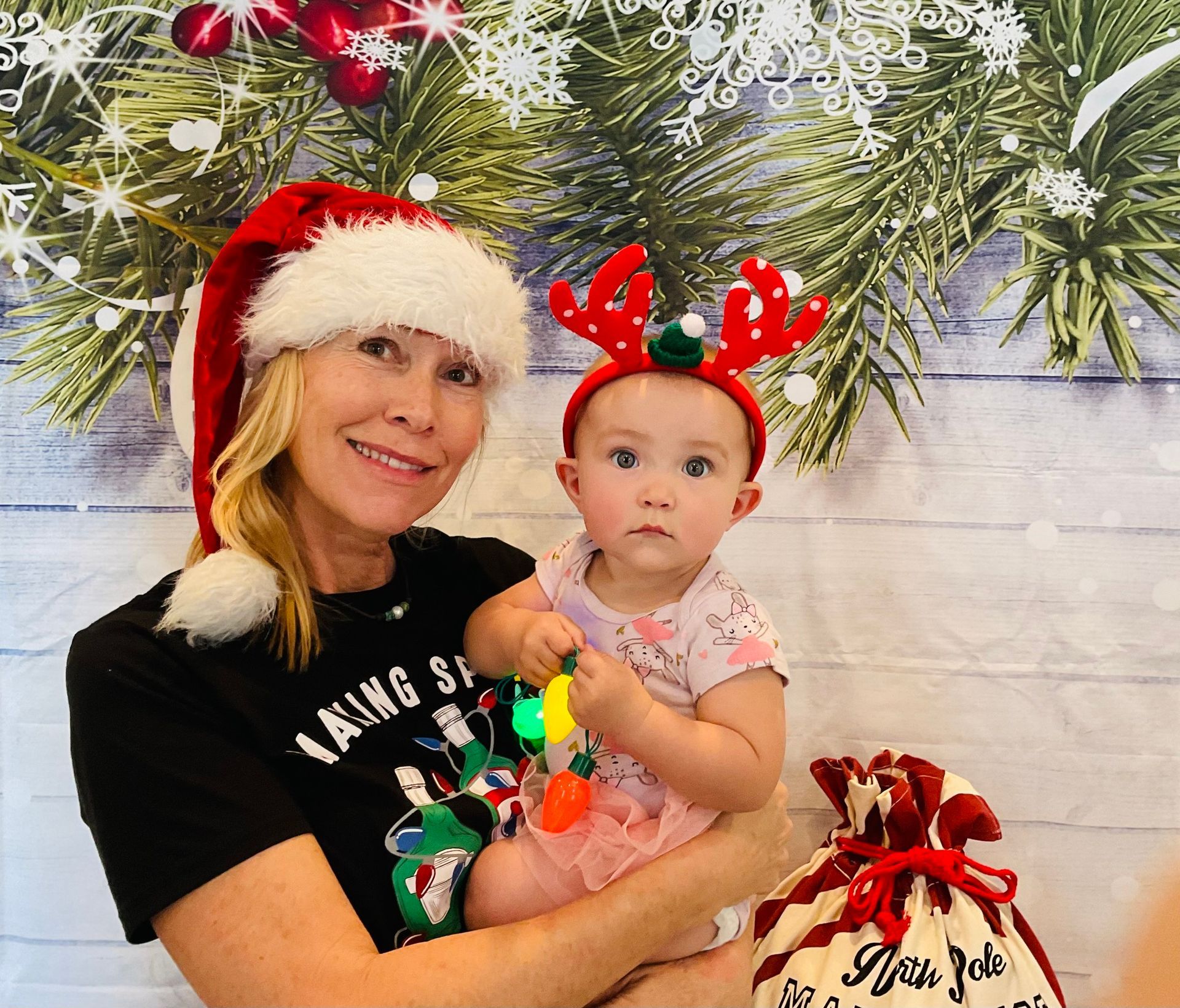 A woman is holding a baby wearing a santa hat and reindeer antlers.