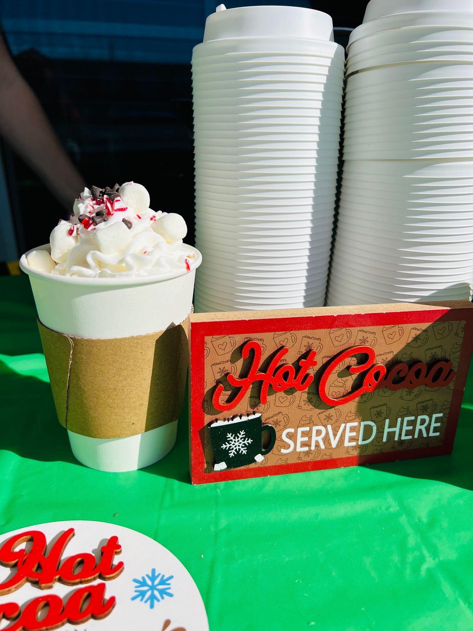 A cup of hot cocoa with whipped cream and a sign that says hot cocoa served here