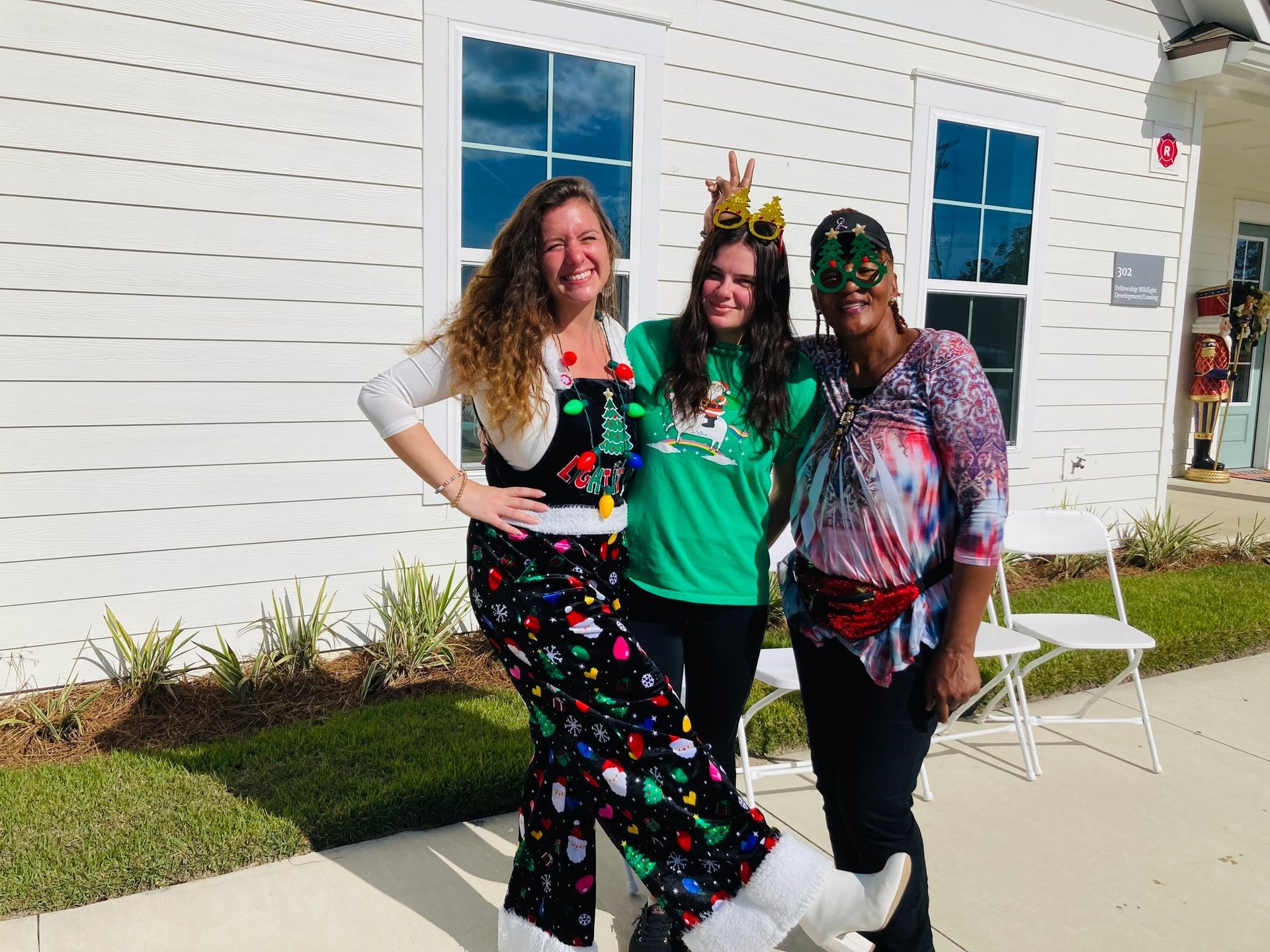 Three women are posing for a picture in front of a white building.