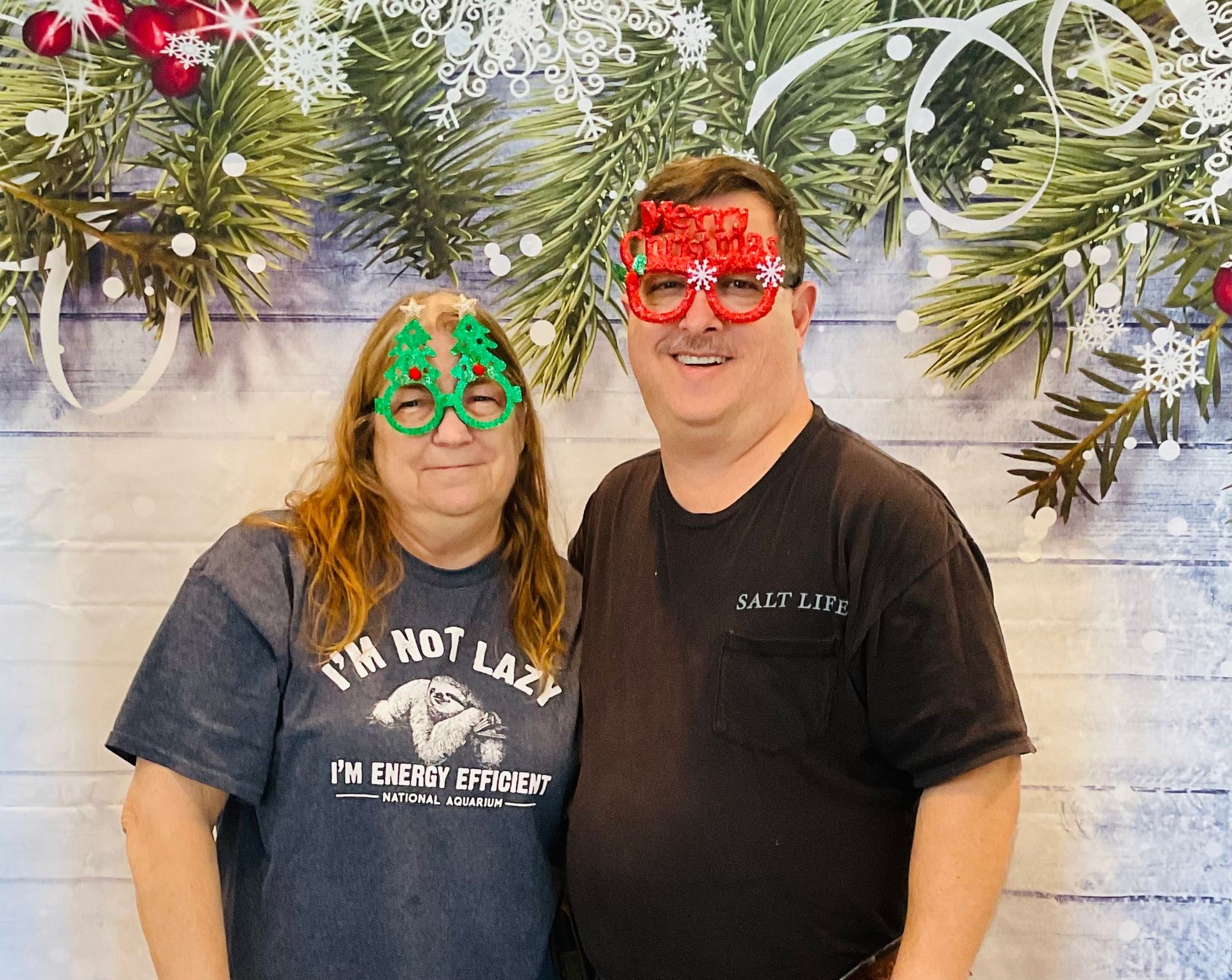 A man and a woman are posing for a picture with christmas decorations in the background.