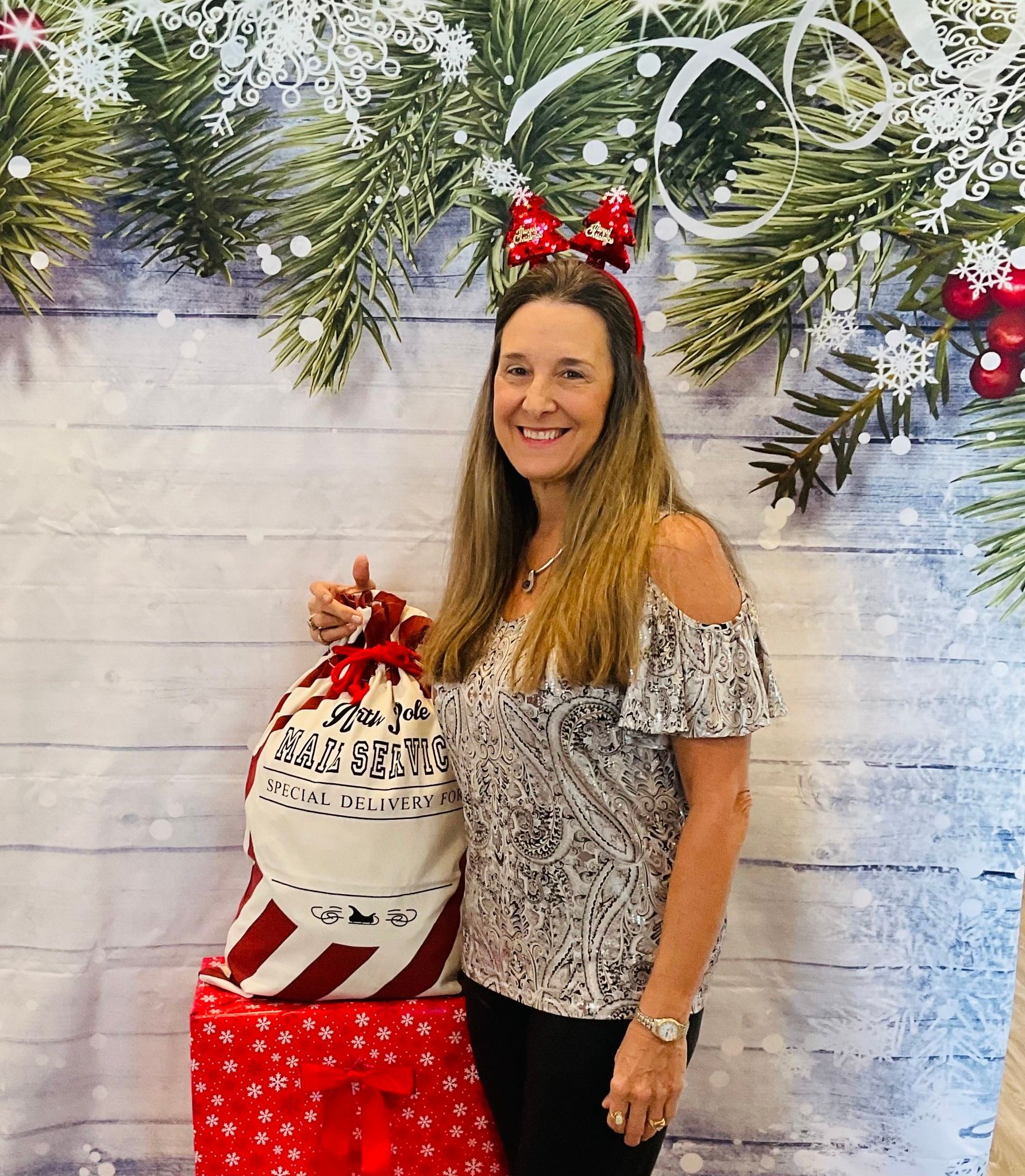 A woman is standing in front of a christmas backdrop holding a christmas bag.