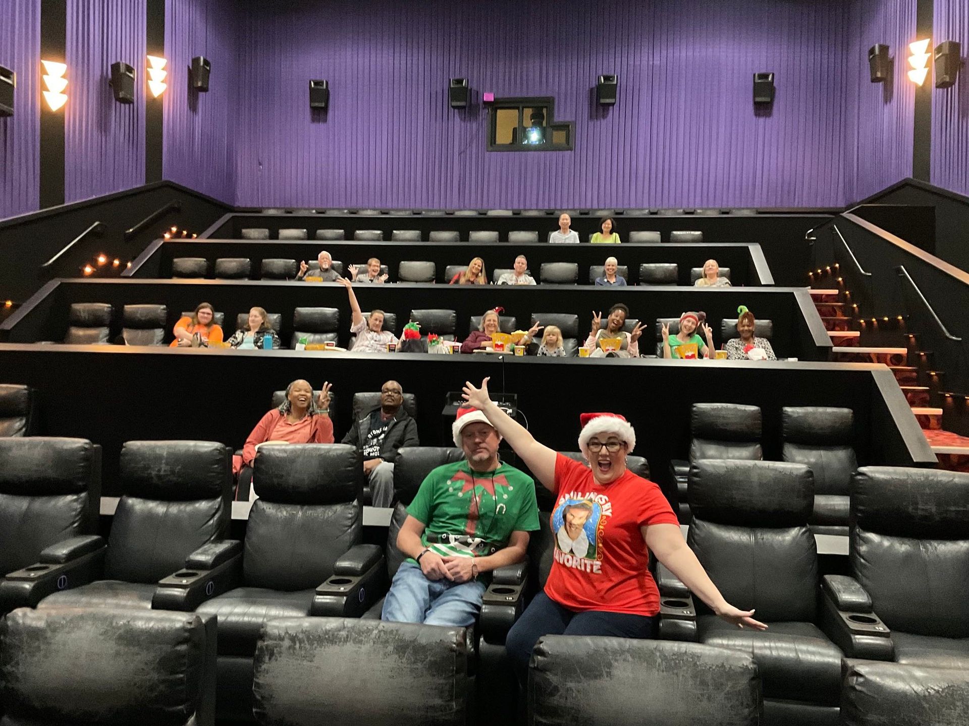 A group of people are sitting in a theater wearing santa hats.
