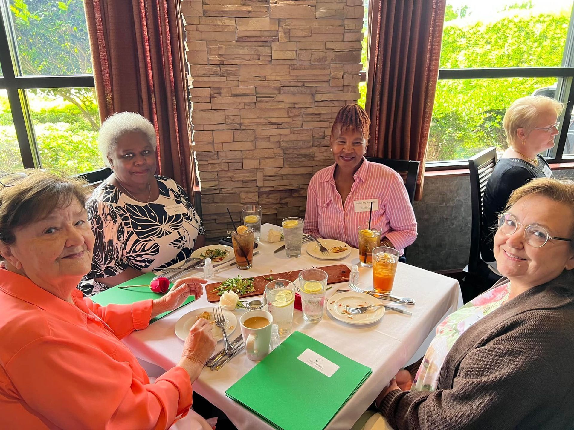 A group of women are sitting at a table with plates of food and drinks.