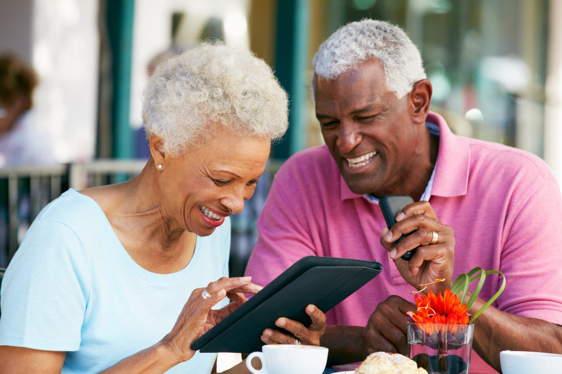 A man and a woman are sitting at a table looking at a tablet.