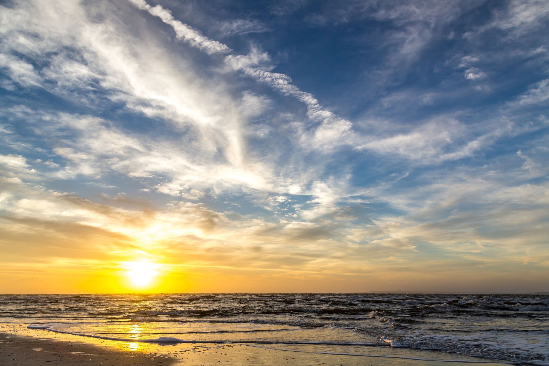 Sunset over the ocean with golden light reflecting on waves under a cloudy sky in Fernandina Beach, FL