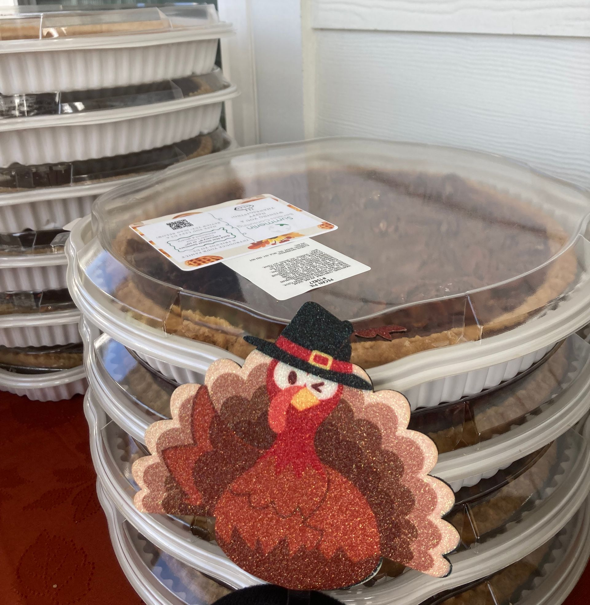 Stacked clear dessert containers with covered pies and a turkey decoration on the front.
