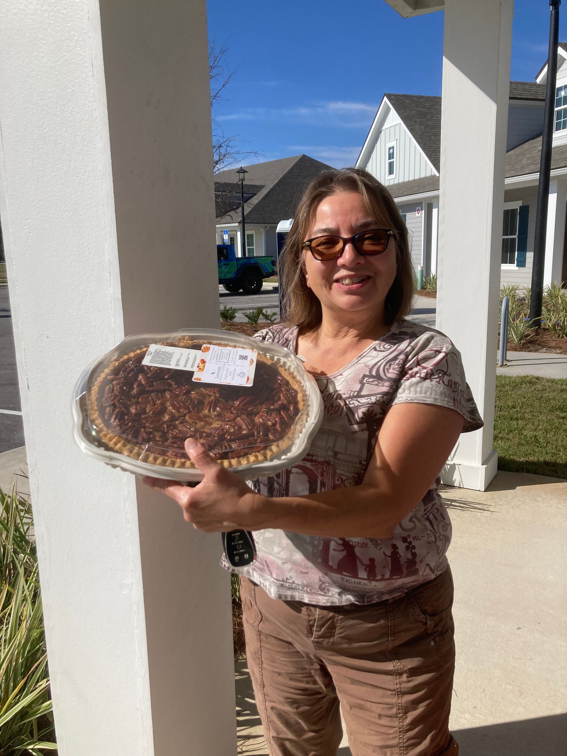 Woman holding a large round cake outdoors on a sunny porch