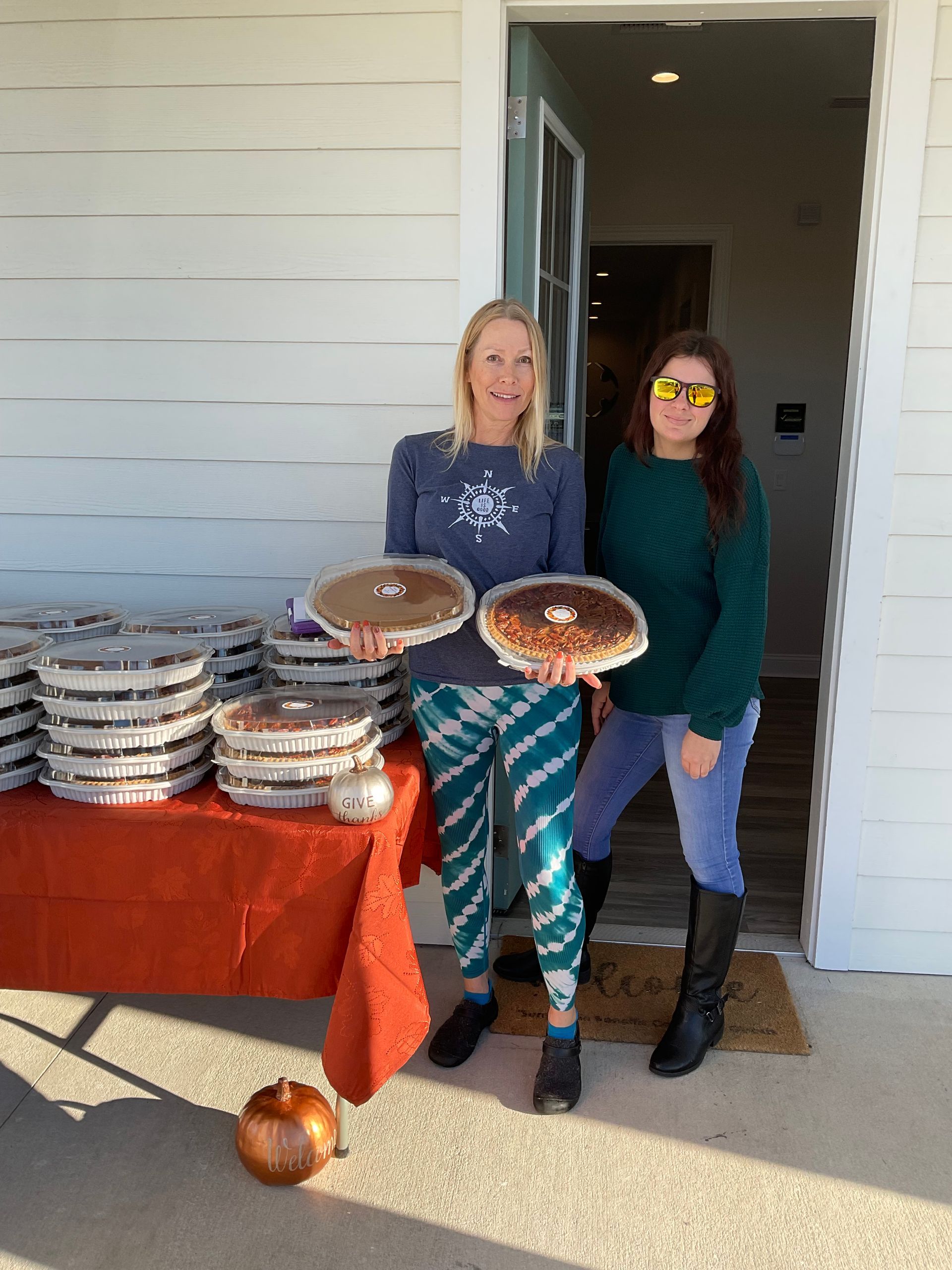 Two women are standing in front of a table holding pies.