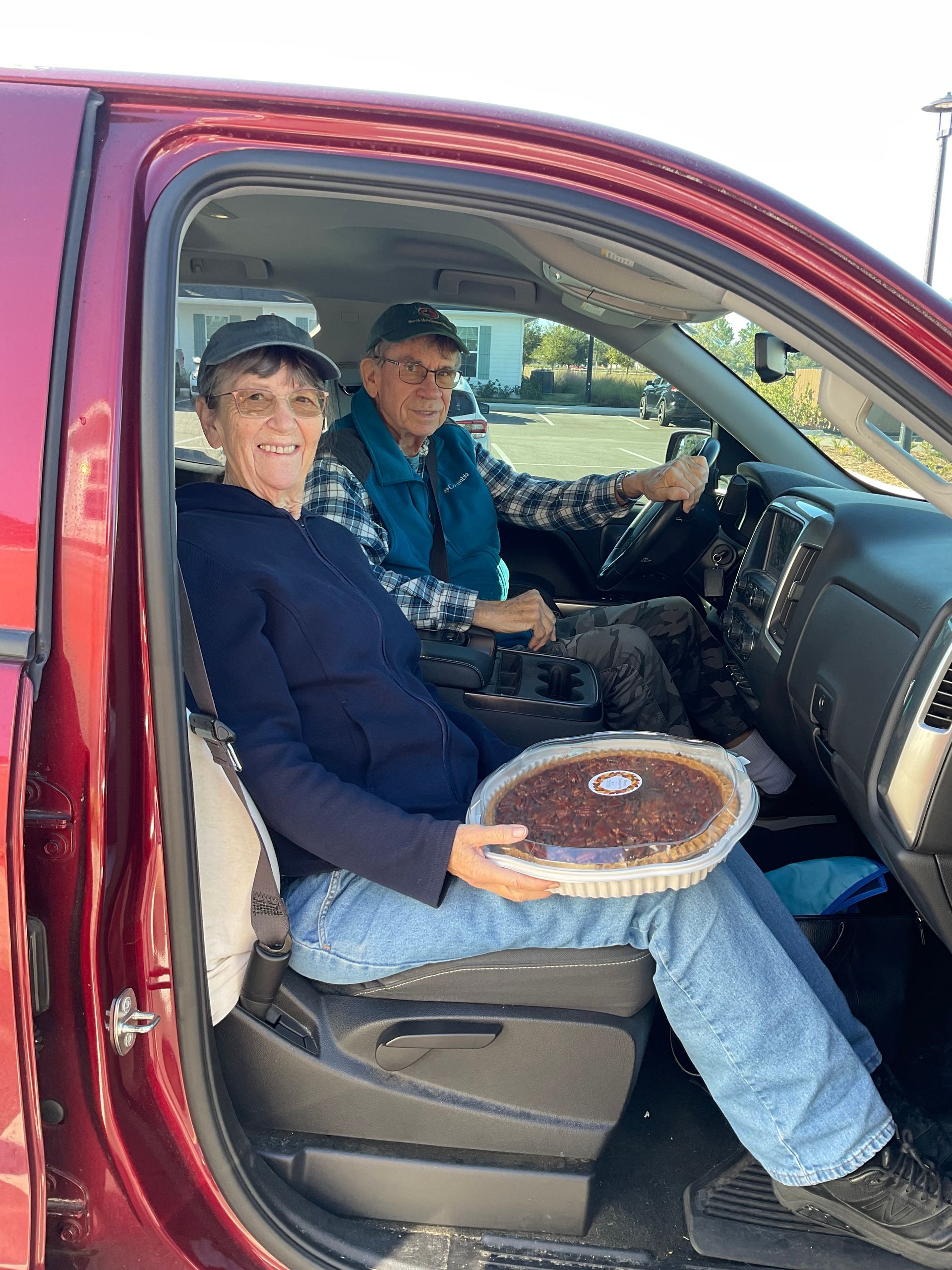 A man and a woman are sitting in the back seat of a truck holding a pie.