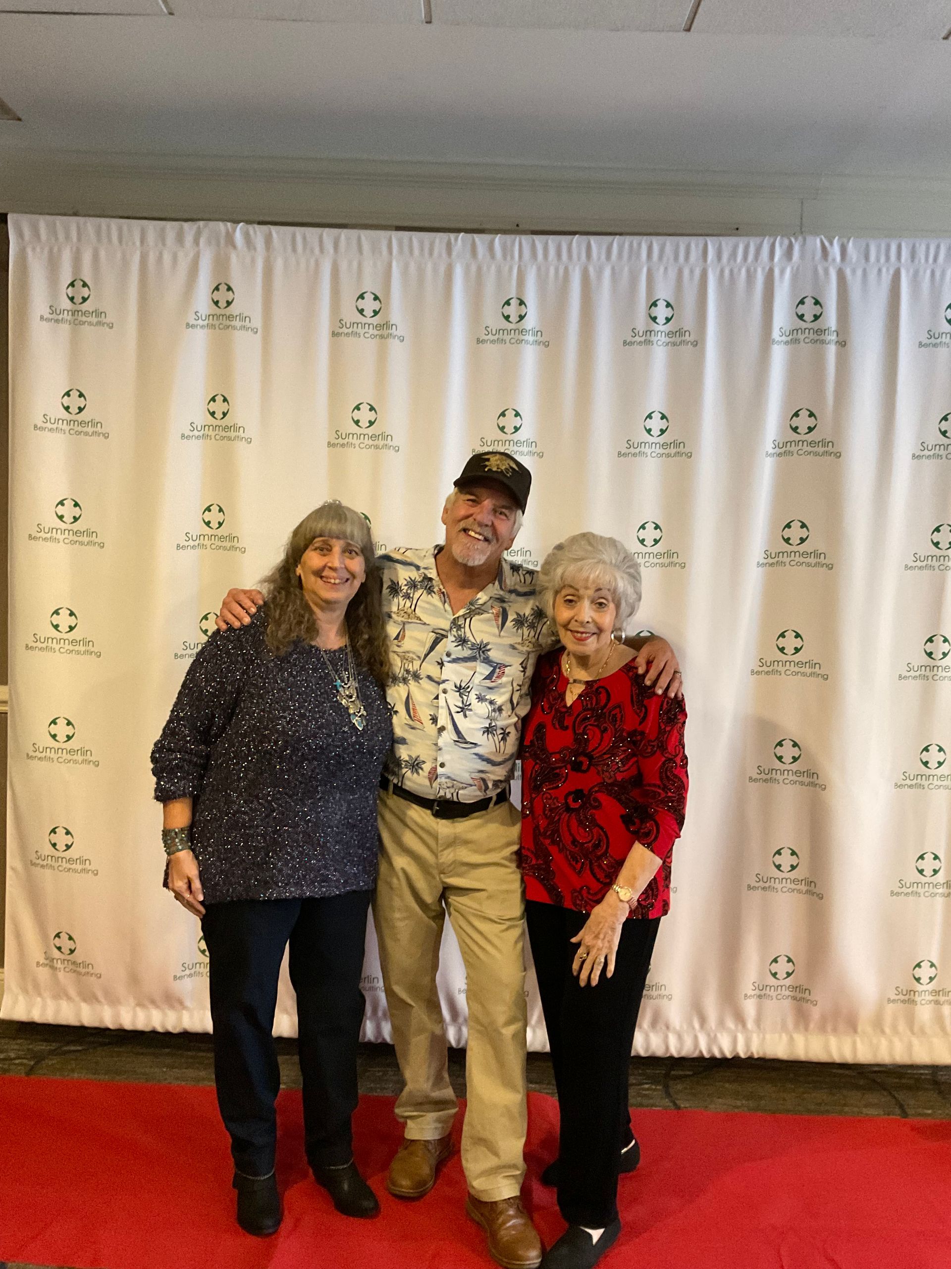 A man and two women are posing for a picture on a red carpet.