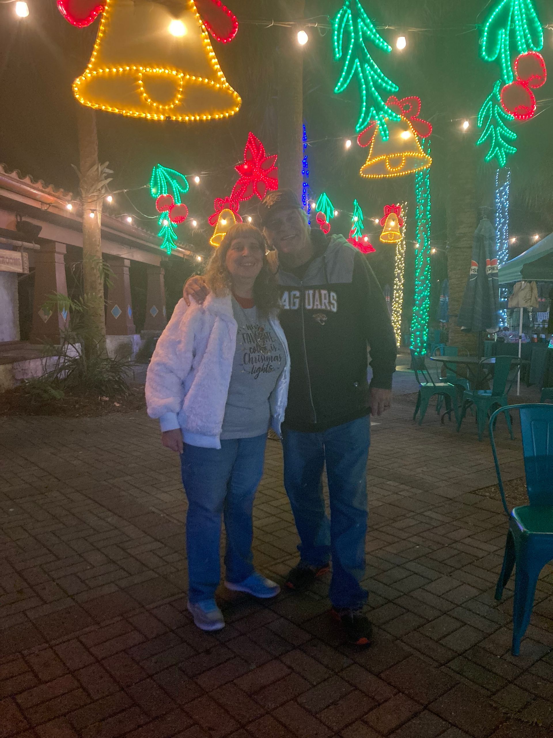 Two people standing together at night under colorful holiday lights in an outdoor plaza