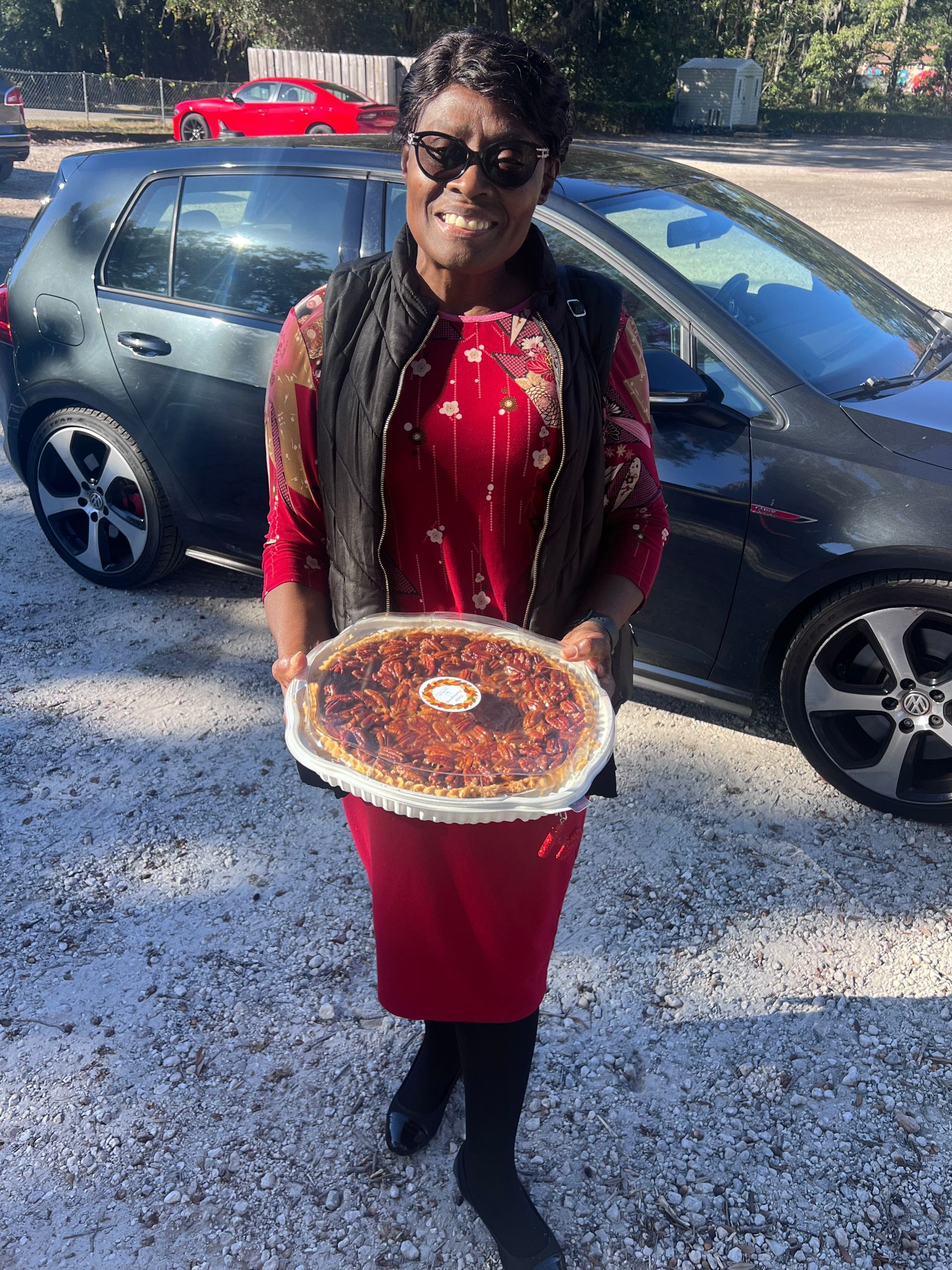 A woman is holding a pizza in front of a car.