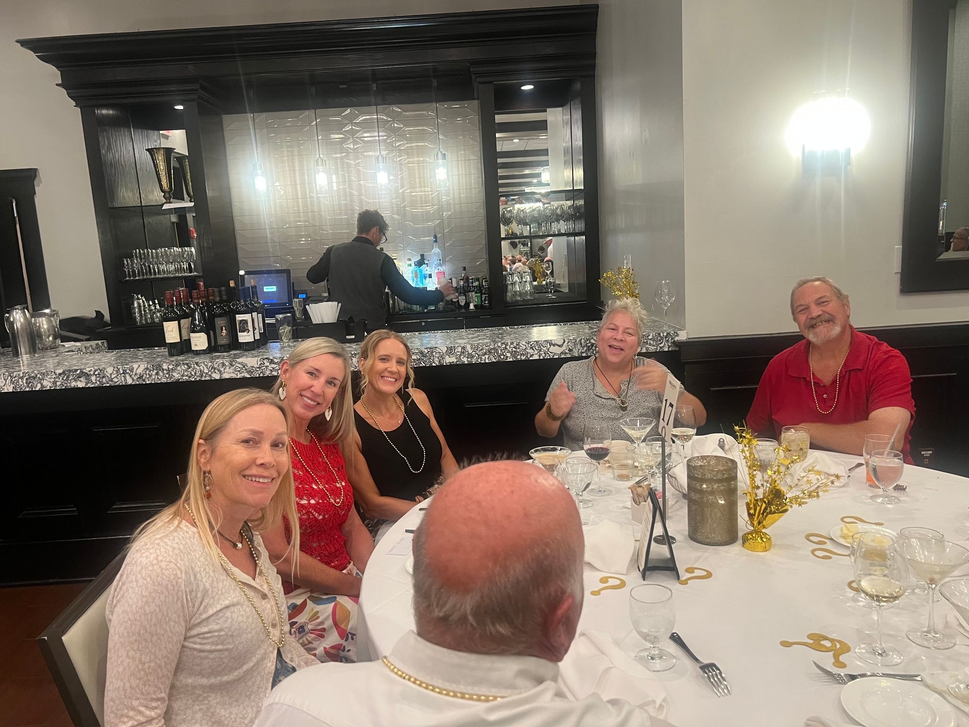Group of people smiling at a table in a restaurant. A bartender is visible behind them.