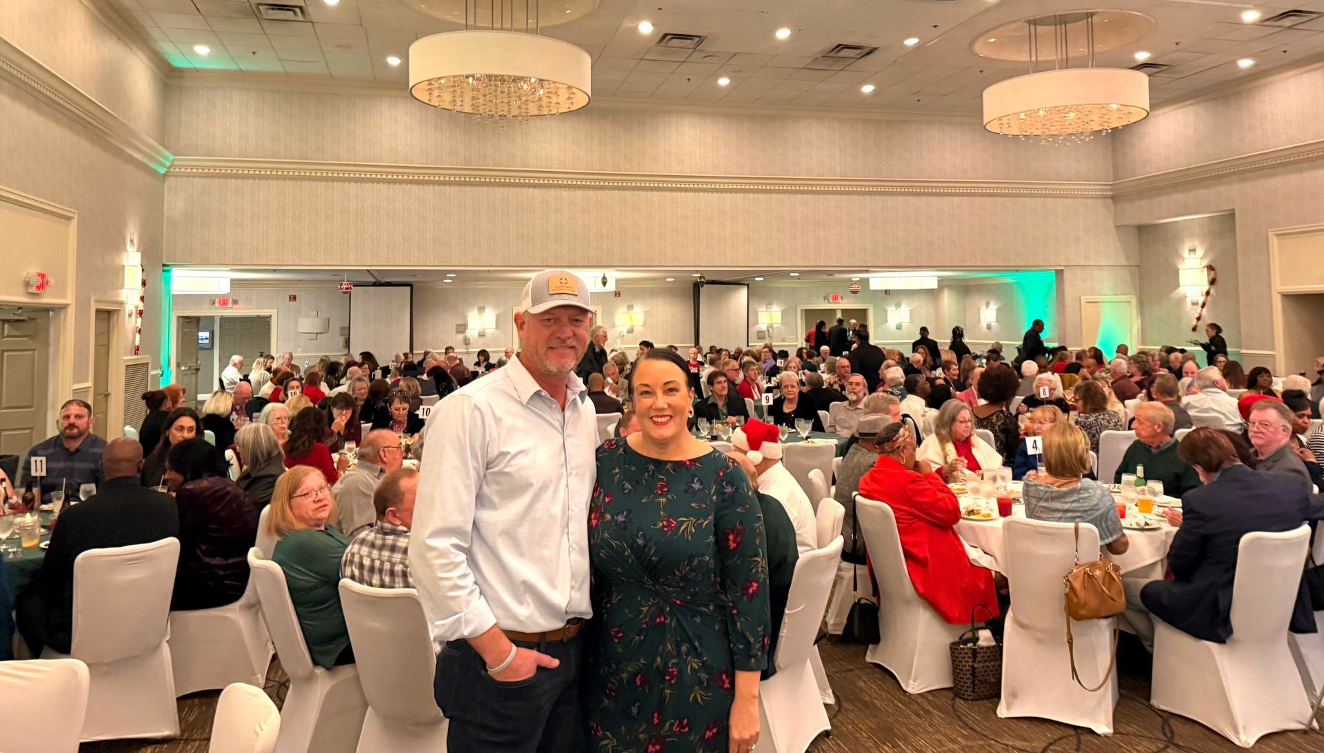 A man and a woman are posing for a picture in a large room filled with people.