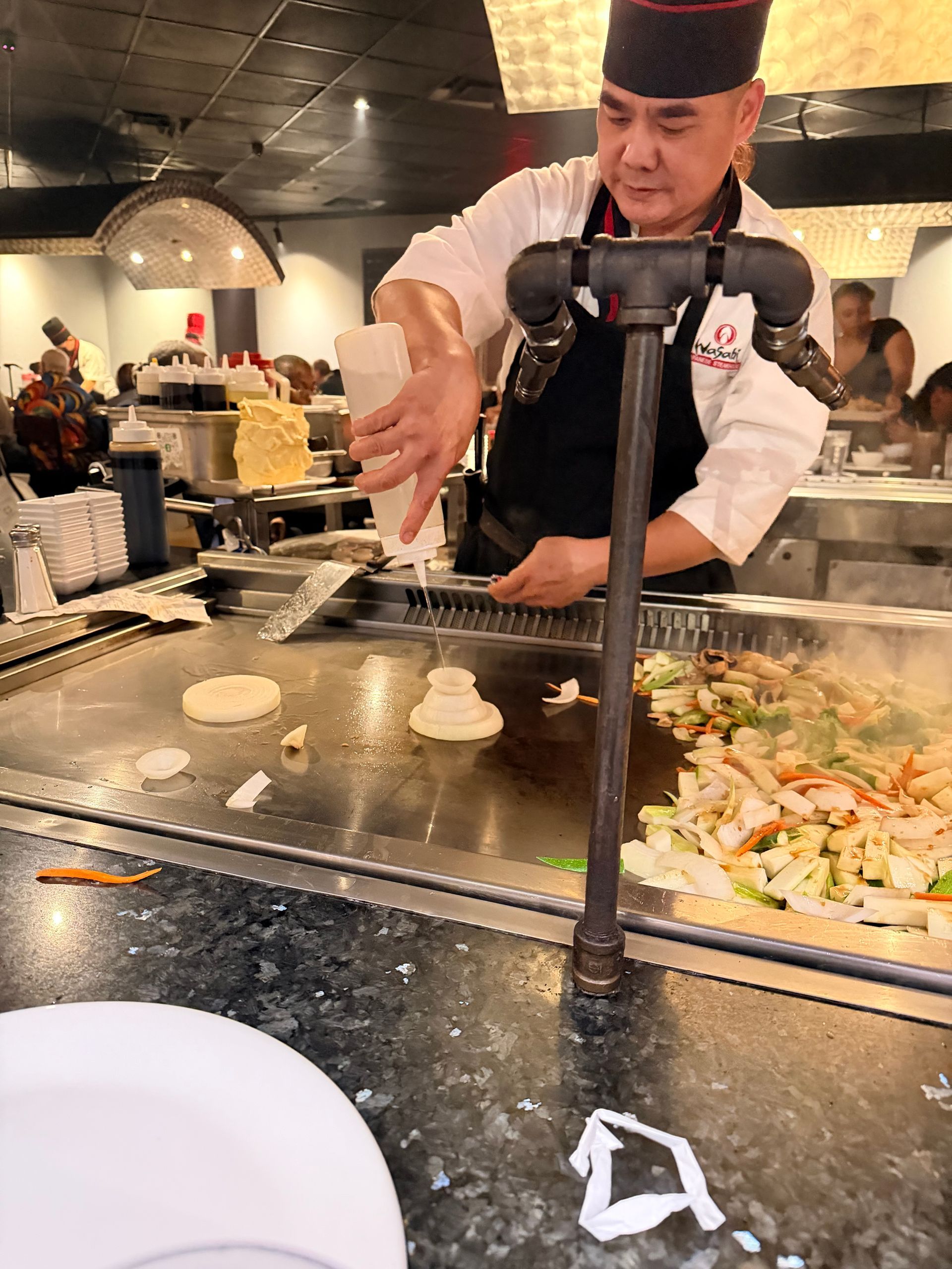 Chef cooking at a hibachi grill, flipping food on a teppanyaki table in a restaurant.